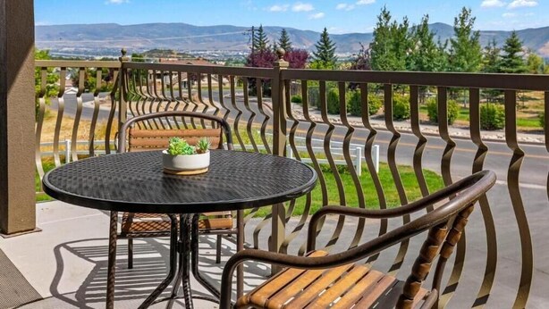 A balcony with a round table and a bench, overlooking a scenic landscape with mountains and trees. - Charming 2-bedroom resort in lovely Midway with gym, indoor pool and more. (Midway)