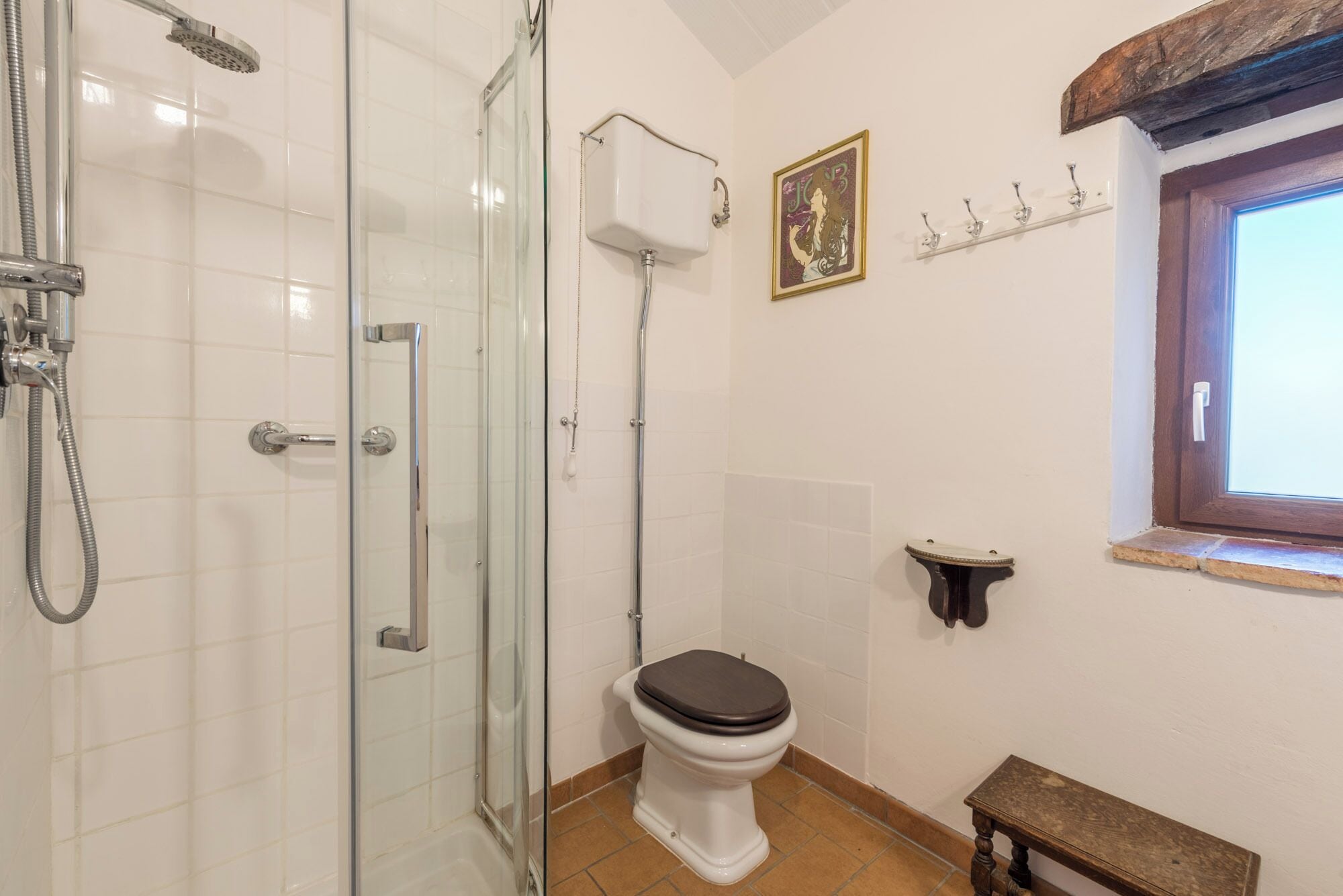 A bathroom with a glass shower enclosure, a white toilet, and a wooden bench.