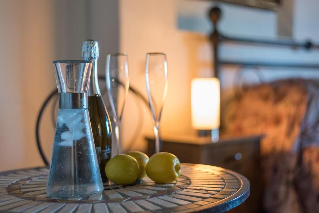 A table with a glass pitcher, a bottle, and two glasses on a mosaic table.