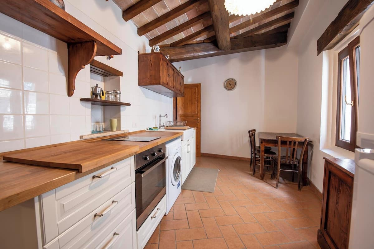 A kitchen with wooden cabinets, a sink, a stove, and a dining area with chairs.