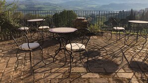 An outdoor patio with stone flooring and metal chairs, overlooking a scenic valley. - Lemon Tree Boutique Guesthouse (Todi)