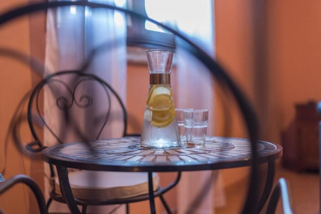 A clear glass pitcher with a lemon slice on a metal table.