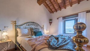 A bedroom with a metal bed frame, a bedside table with a lamp, a window with curtains, and a view of the sea. - Lemon Tree Boutique Guesthouse (Todi)