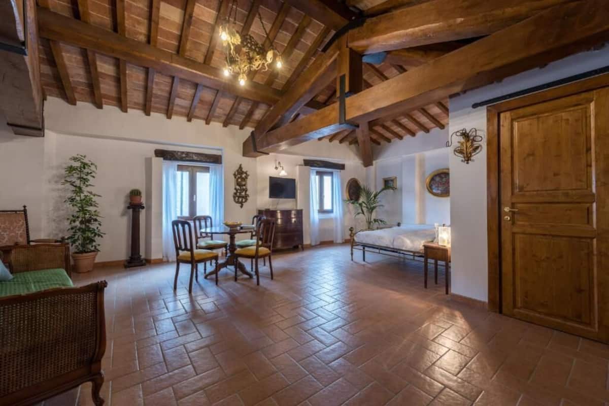 A rustic room with a wooden ceiling, a bed, a dining table with chairs, and a wooden wardrobe.