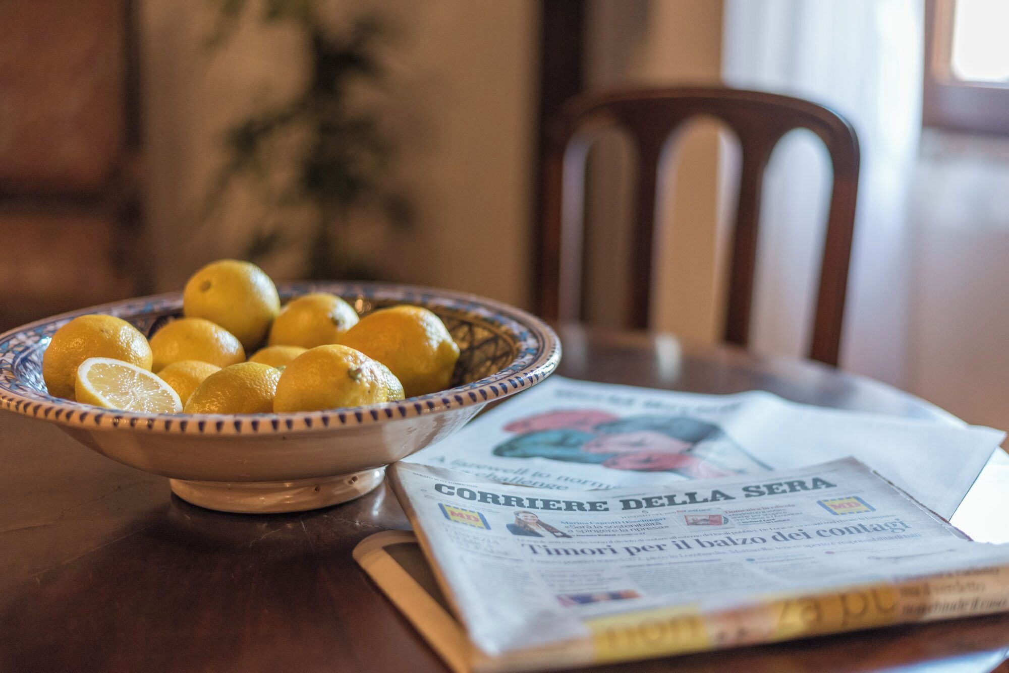 A bowl of lemons on a table with a newspaper.