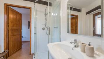 Une salle de bain moderne avec une douche à parois de verre, un grand lavabo doté de deux distributeurs de savon et un miroir au-dessus du lavabo.