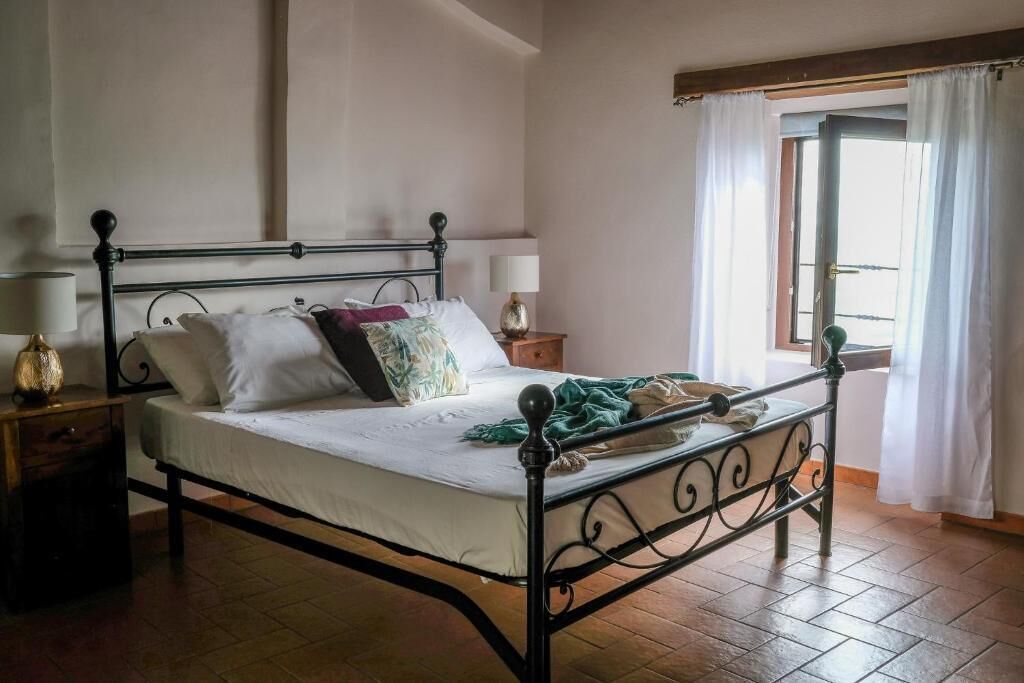 Een slaapkamer met een metalen bedframe, een houten nachtkastje met een lamp en een raam met gordijnen.