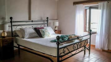 Een slaapkamer met een metalen bedframe, een houten nachtkastje met een lamp en een raam met gordijnen.