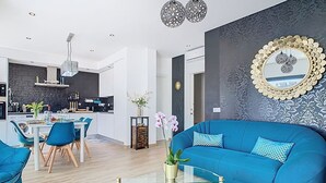 A modern living room with a blue sofa, a glass coffee table, and a kitchen in the background. - Casa Launa Fuseta (Moncarapacho)
