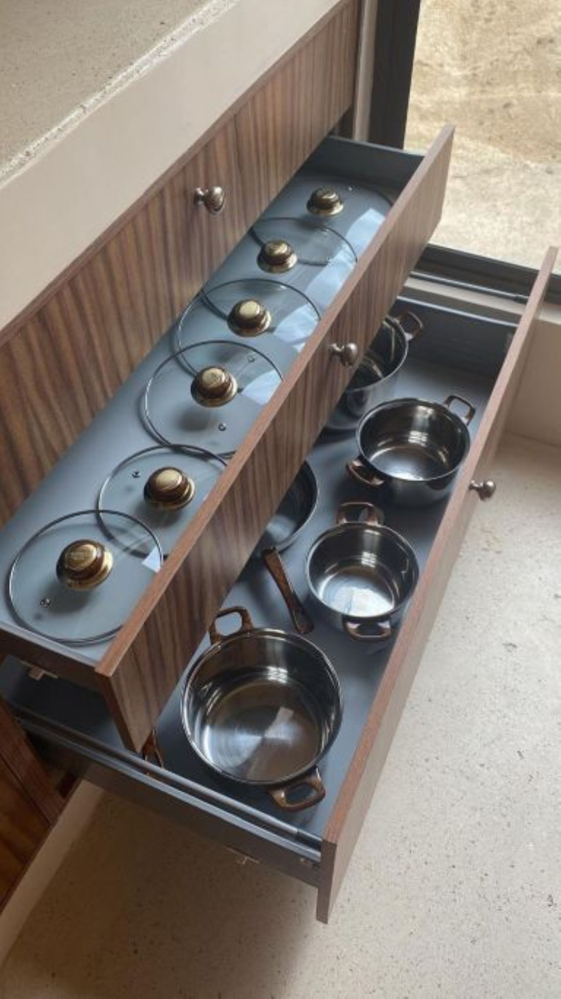 A kitchen with a built-in stove and a drawer with pots and pans.