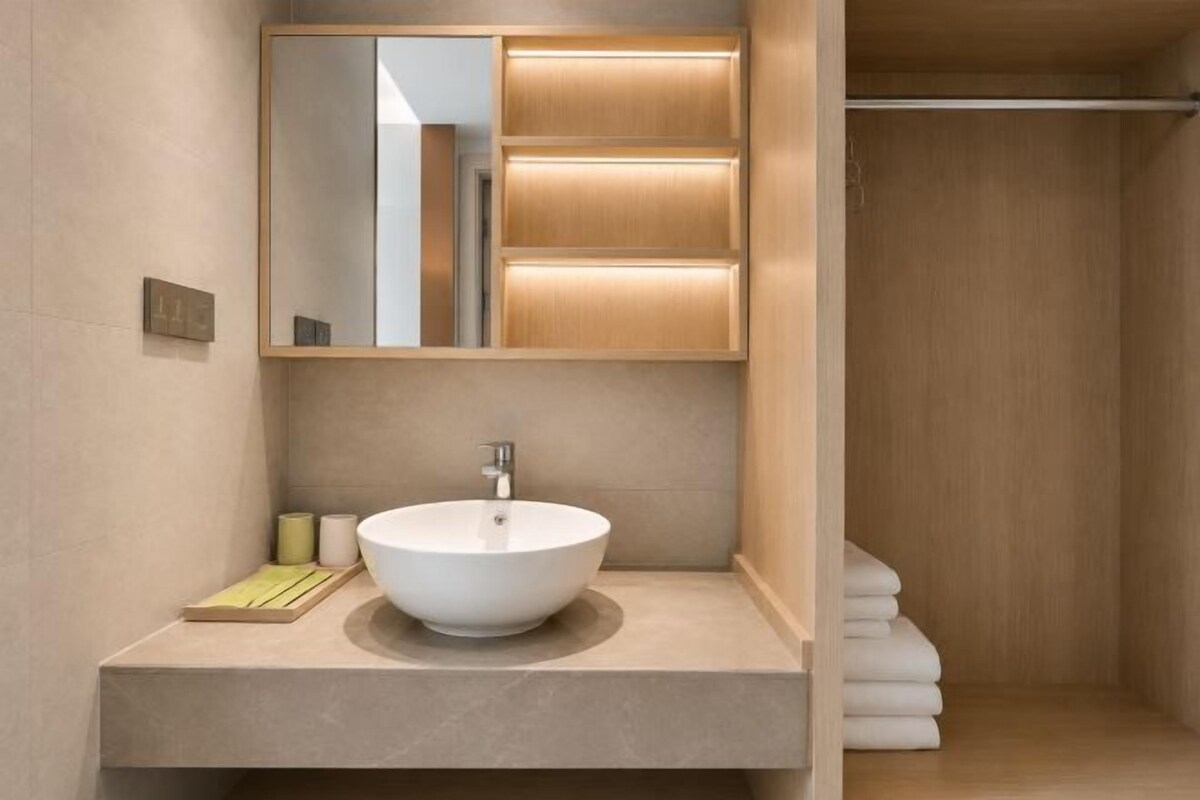 A modern bathroom with a large mirror, a round sink, and a wooden vanity.