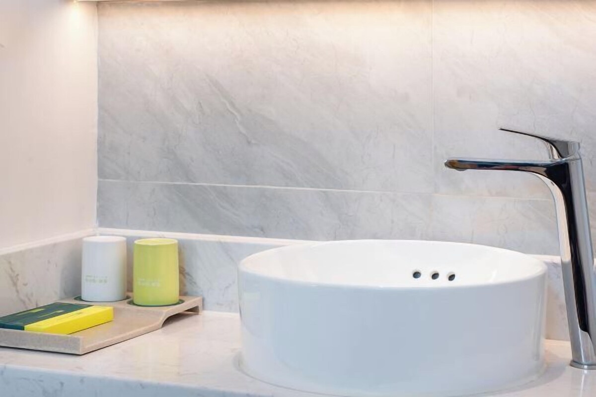 Un bagno con un lavandino bianco, un rubinetto moderno e due contenitori cilindrici su un vassoio.