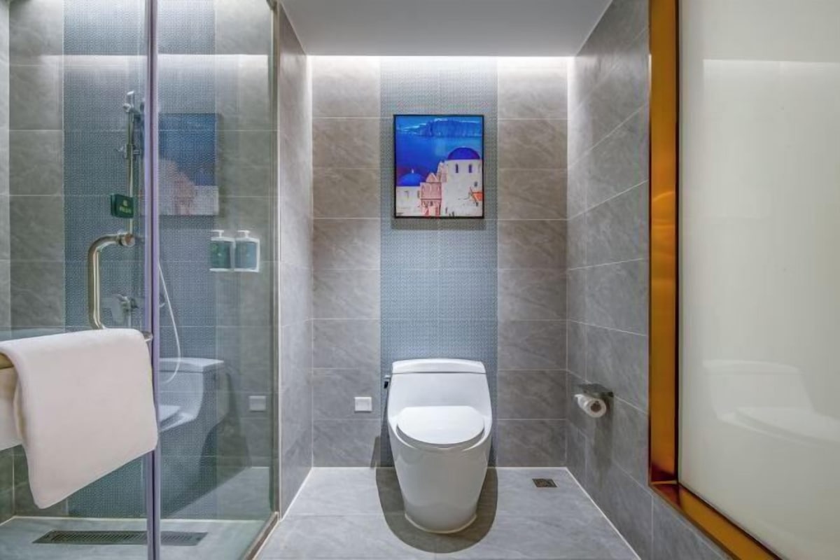 A modern bathroom with a glass shower enclosure, a toilet, and a framed picture on the wall.