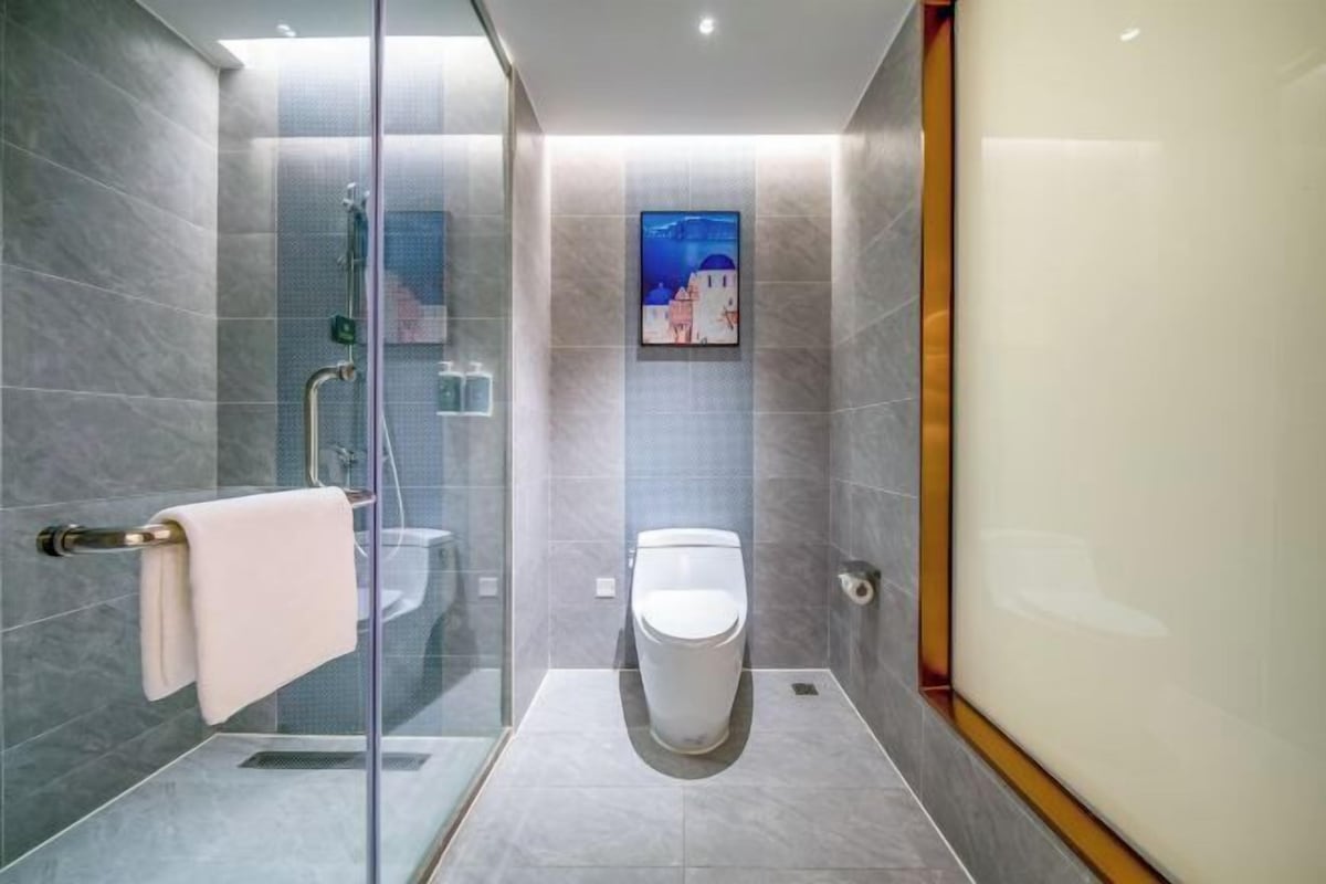 A modern bathroom with a glass-enclosed shower, a toilet, and a framed picture on the wall.