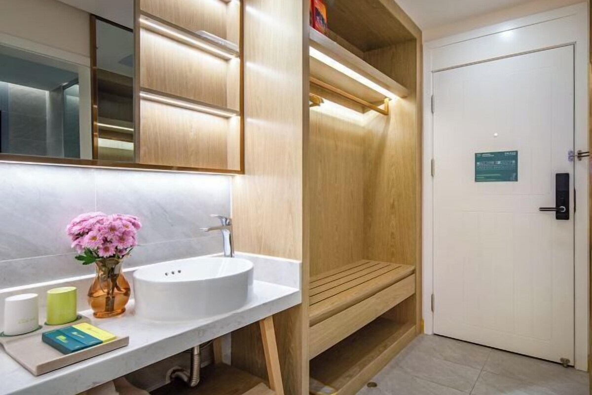 A modern bathroom with a white sink, a mirror, a wooden bench, and a white door with a sign.