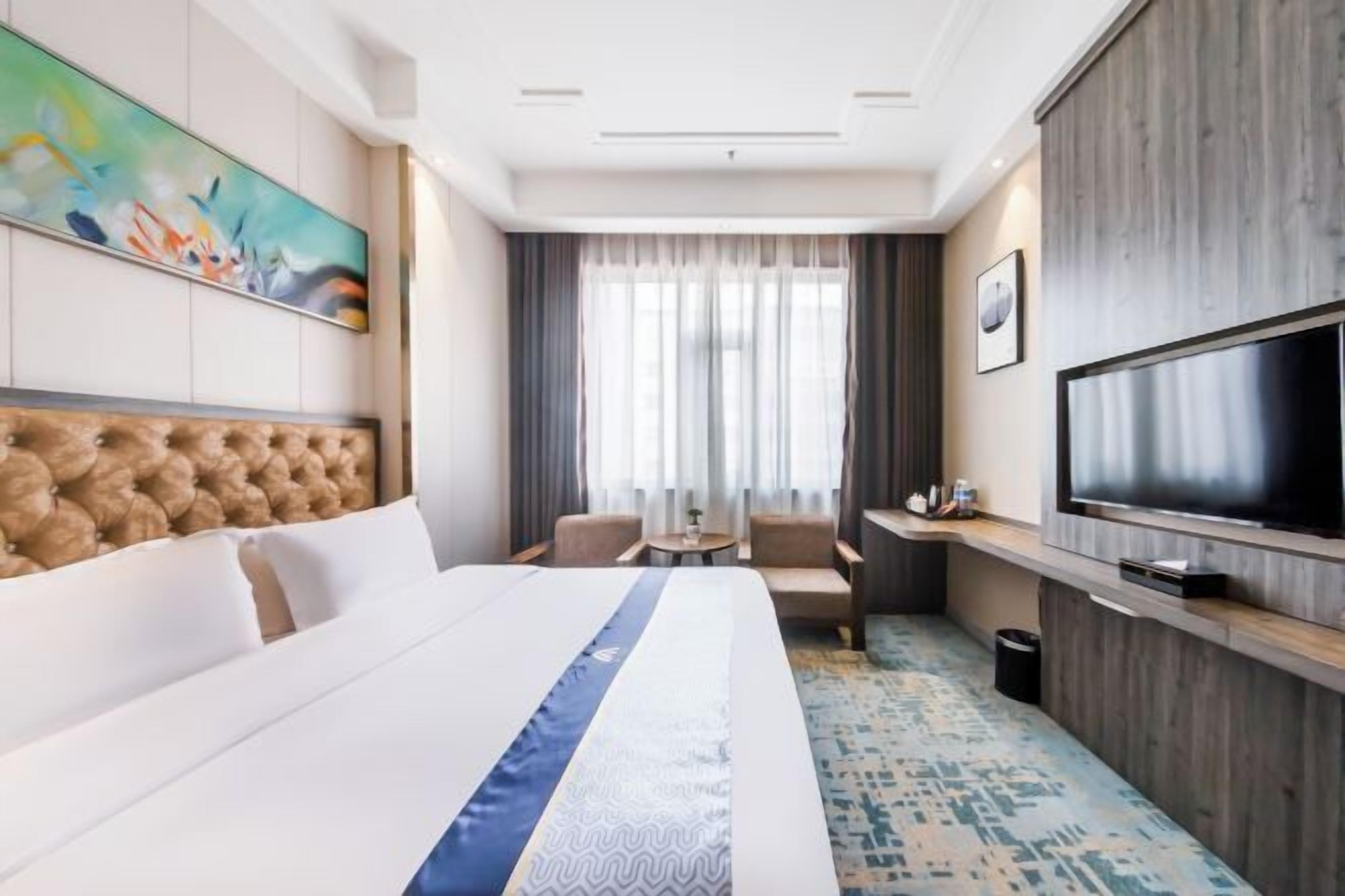 Una habitación de hotel con una cama grande, un televisor de pantalla plana, un escritorio con una silla y un cuadro en la pared.