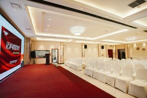Une salle de conférence avec un tapis rouge, des chaises blanches, un pupitre et un grand écran.