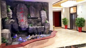 Un hall d’entrée agrémenté d’une cascade artificielle en roche, d’un comptoir de réception et de plantes en pot.