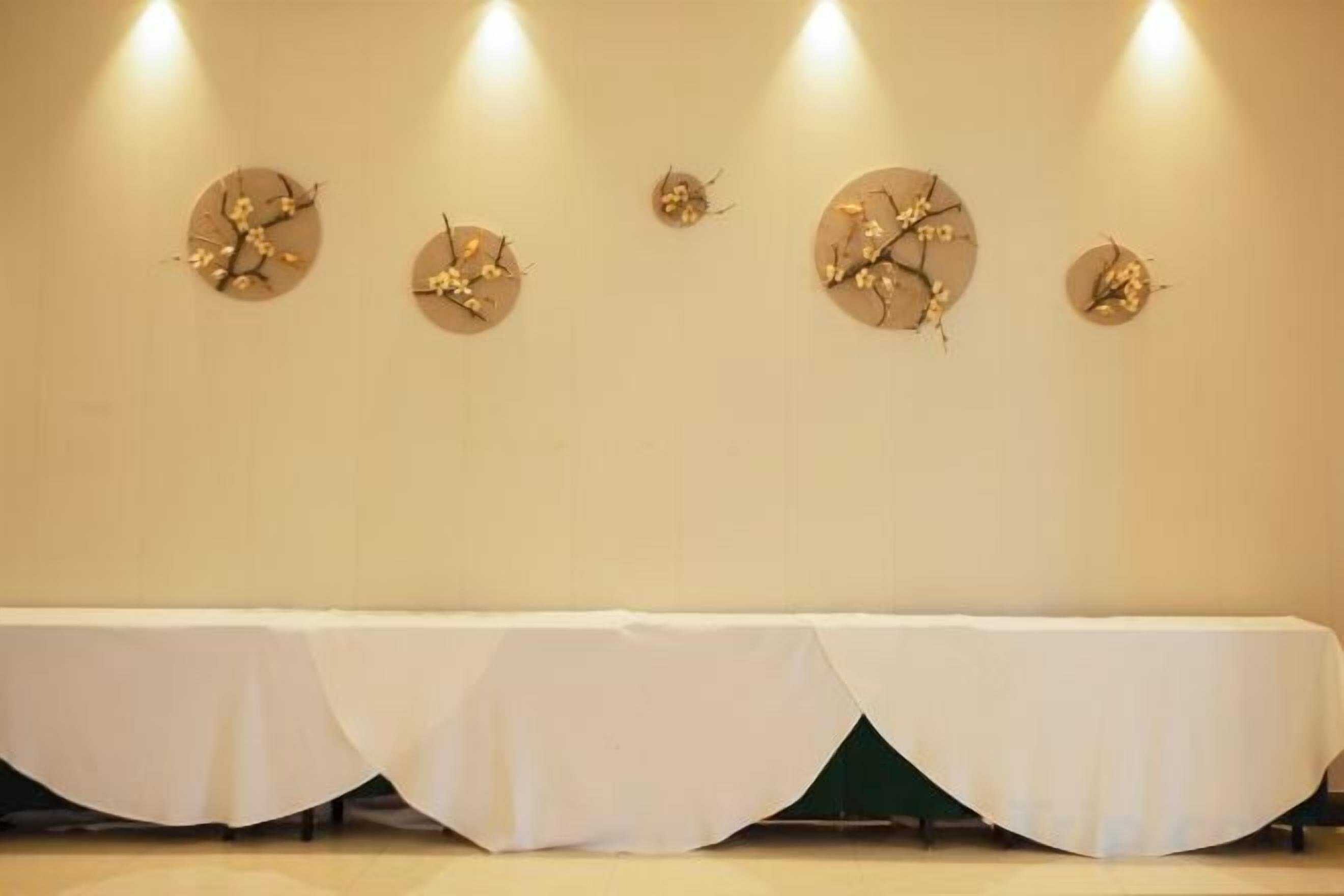 A room with a long table covered with a white tablecloth, four wall-mounted clocks, and recessed lighting.