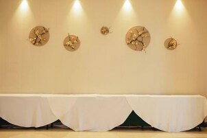 Una habitación con una mesa larga cubierta con mantel blanco, cuatro relojes en la pared e iluminación empotrada.