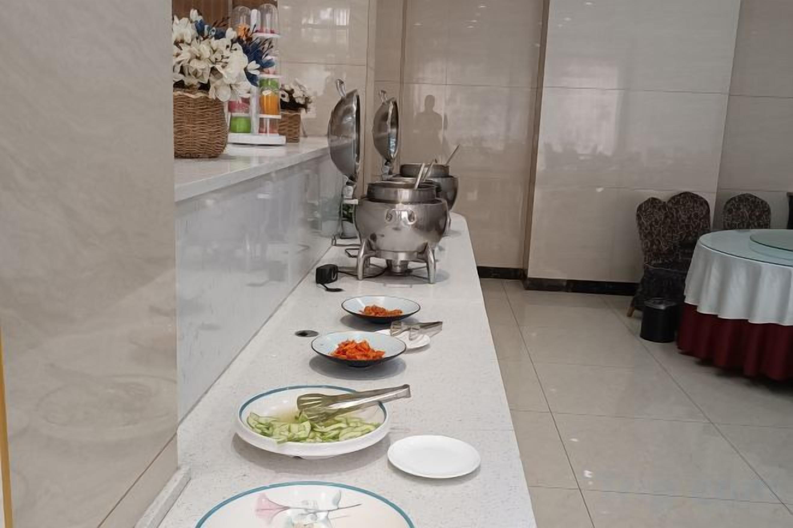 A buffet setup with various dishes and utensils on a long table, a stove, and chairs around a round table.