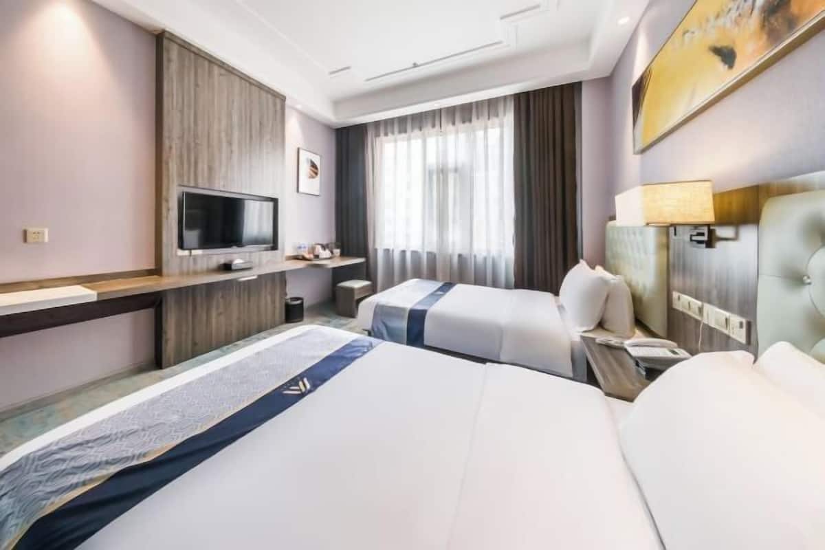 Habitación de hotel con dos camas, televisión, escritorio y ventana con cortinas.