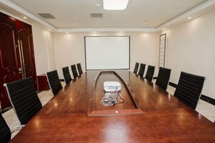 Un salón de conferencias con una larga mesa, sillas, una pantalla de proyector y una pizarra.