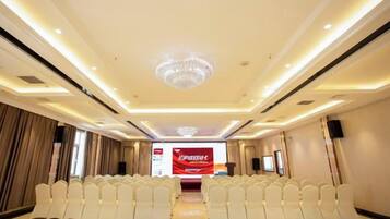 A conference room with rows of white chairs, a chandelier, and a red banner.