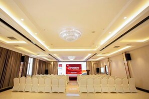 A conference room with rows of white chairs, a chandelier, and a red banner.