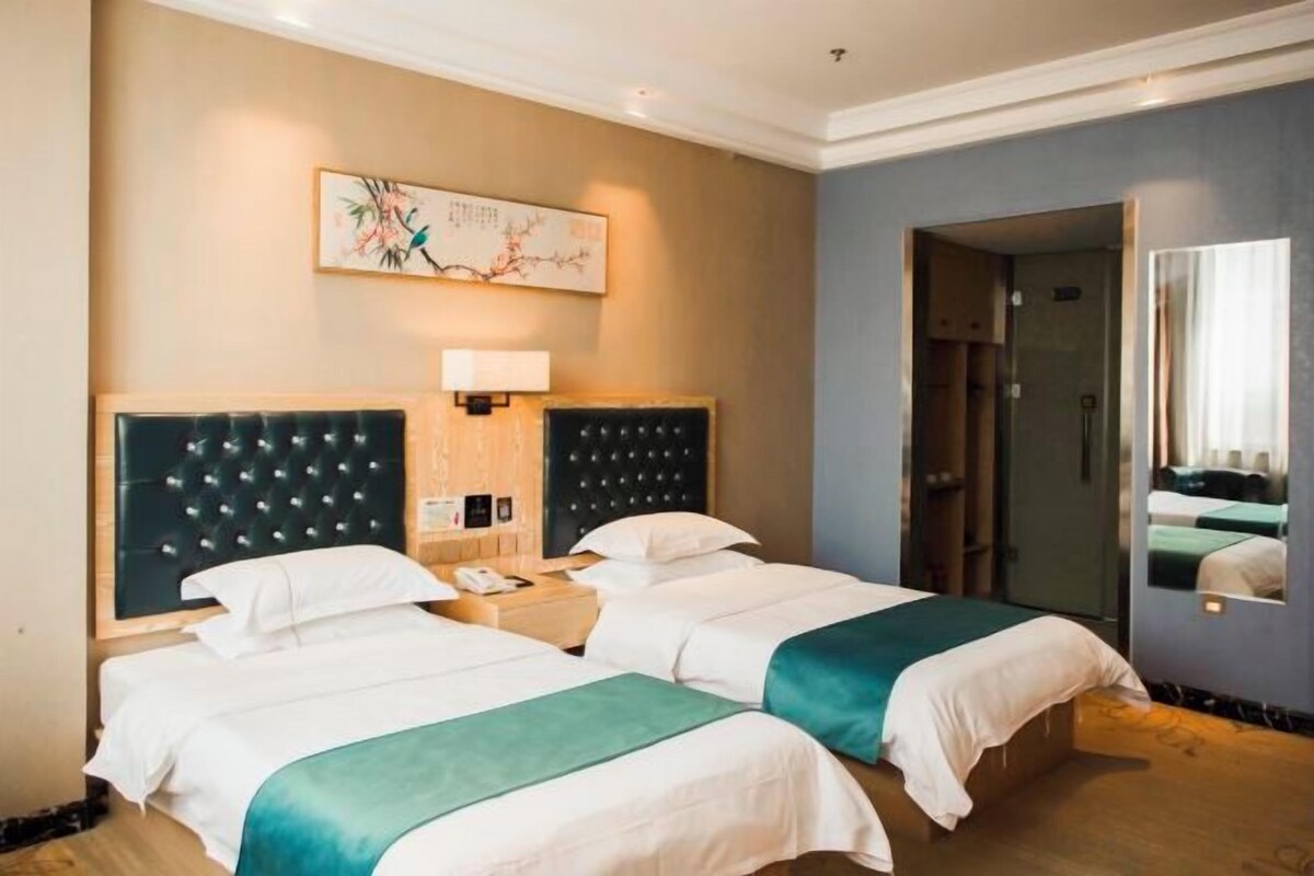Een hotelkamer met twee bedden, een grote spiegel, een kunstwerk aan de muur en een deur naar een badkamer.