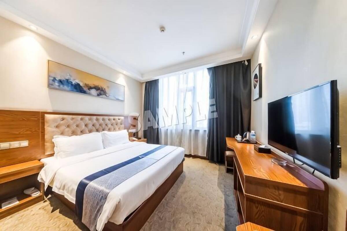 Habitación de hotel con una cama grande, televisión, escritorio y ventana con cortinas.