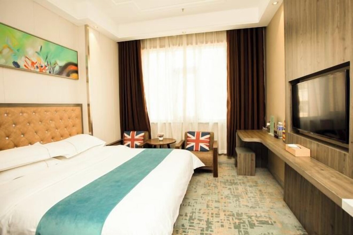 Een hotelkamer met een groot bed, een televisie, een klein tafeltje en een raam met gordijnen.