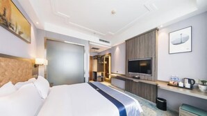 Une chambre d’hôtel avec un grand lit, une télévision, un bureau avec une chaise et une petite poubelle.