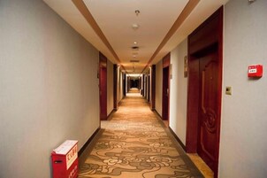 Pasillo de hotel con puertas a ambos lados, alfombra estampada y una caja de alarma contra incendios a la izquierda.