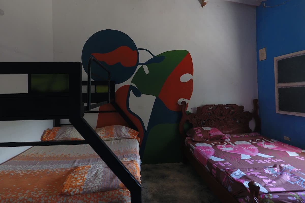 A room with bunk beds, a colorful abstract wall mural, a window, and a bed with a patterned bedspread.