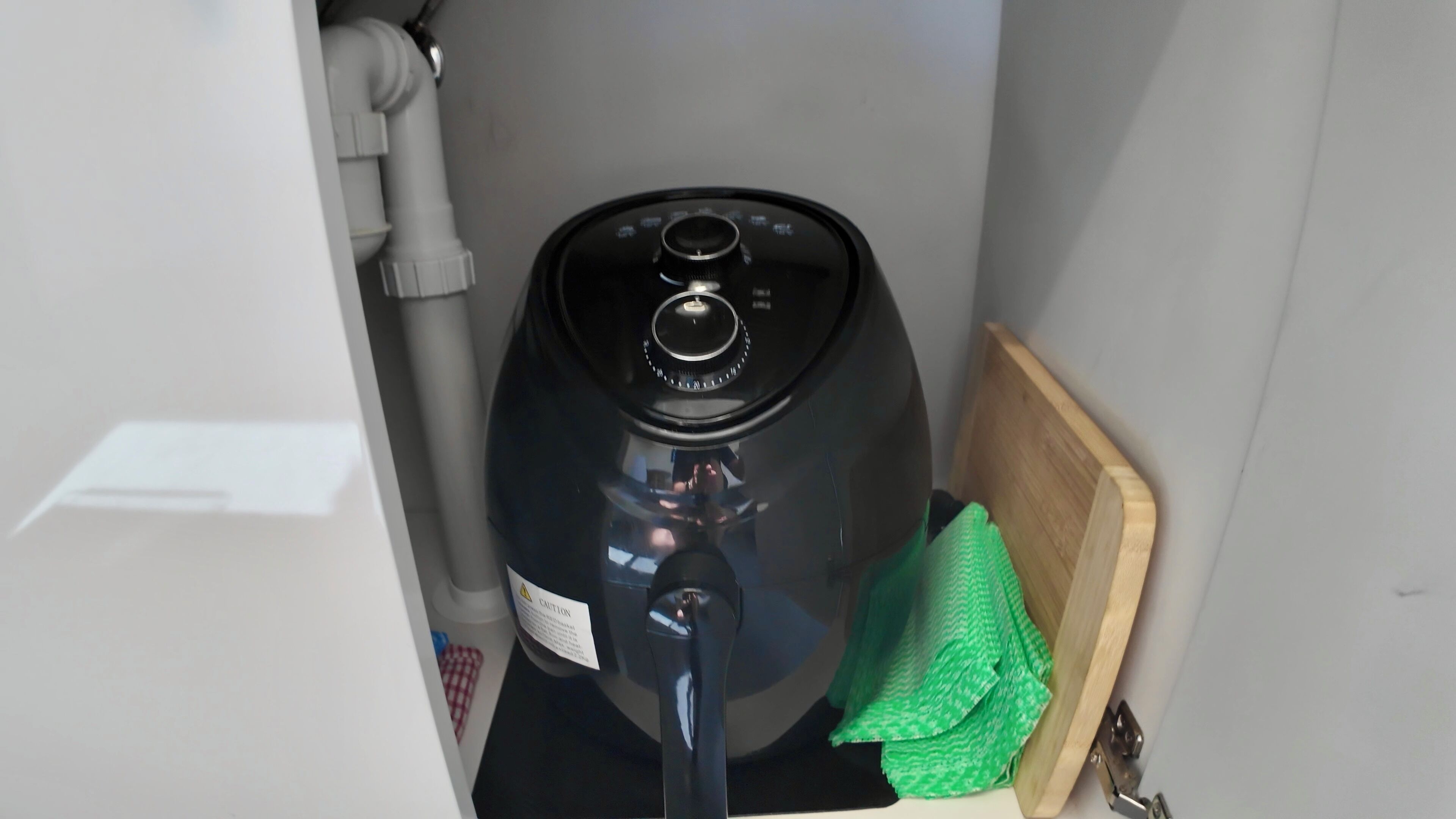 Une cuisine moderne et compacte, avec un appareil électroménager noir, une planche à découper en bois et un torchon vert.