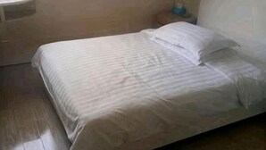 A bed with a striped bedspread and pillows, a wooden floor, and a nightstand with a blue object on it. - Fanchang Ziyuan Express Hotel (Wuhu)