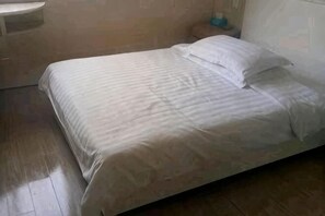 Una cama con cubrecama y almohadas a rayas, piso de madera y mesita de noche con un objeto azul encima.