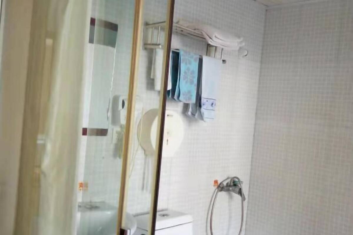 A bathroom with a glass partition, a toilet, a towel rack with towels, and a shower area.