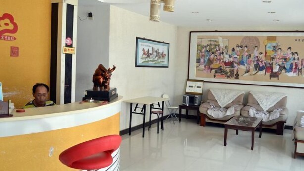 A hotel reception area with a counter, a receptionist, a sofa set, and a large painting on the wall. - Fanchang Ziyuan Express Hotel (Wuhu)
