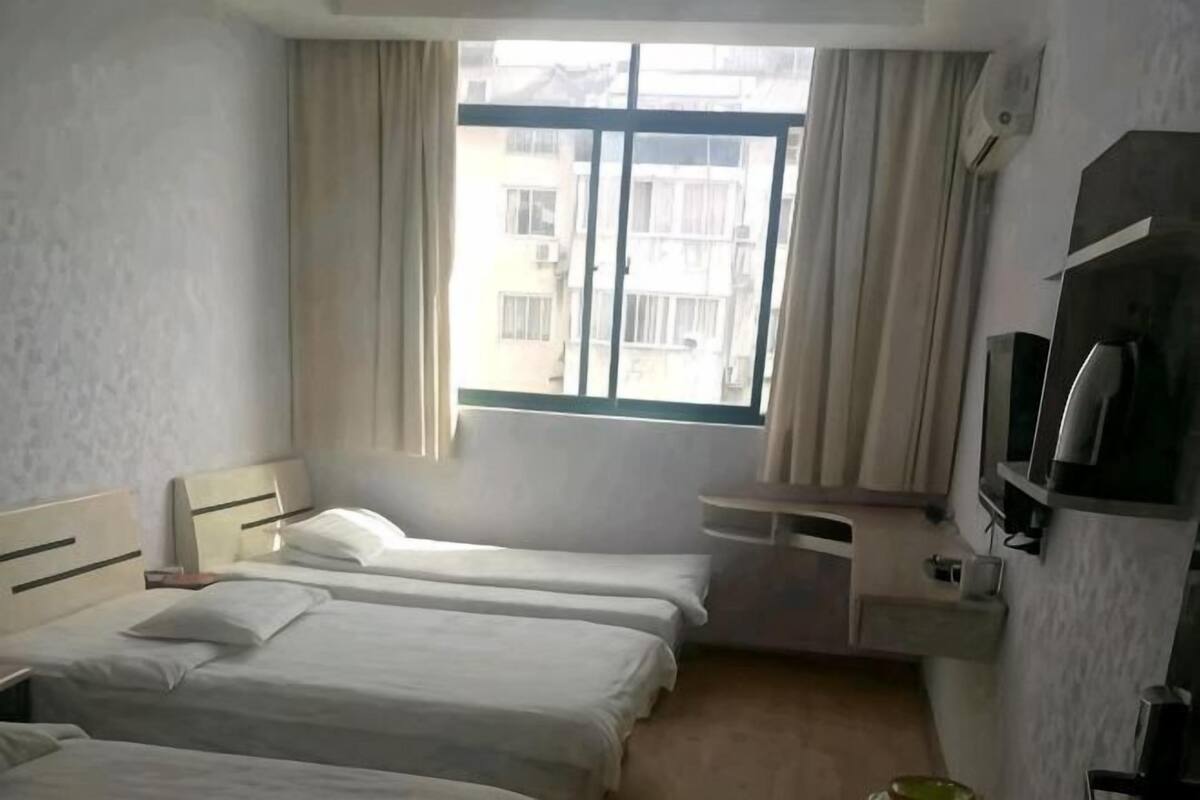 A hotel room with two beds, a desk, a TV, and a window with curtains.