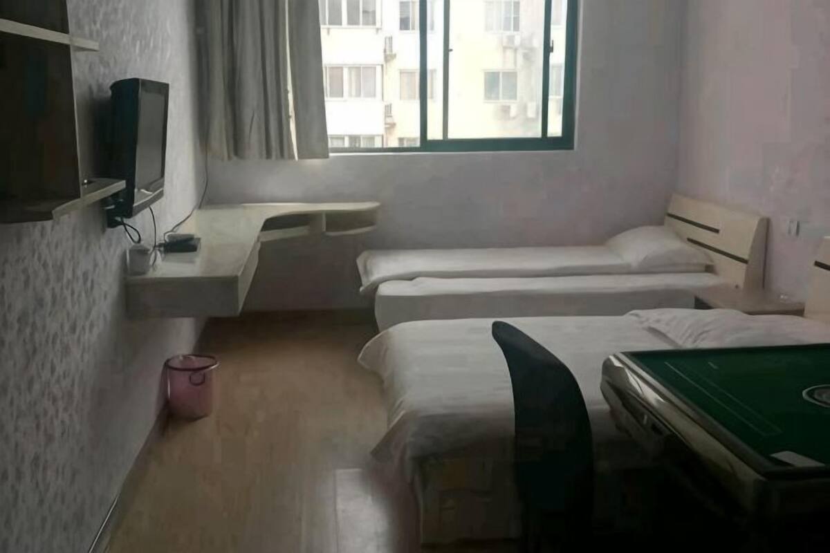 A room with two beds, a desk, a television, and a window with a view of buildings.