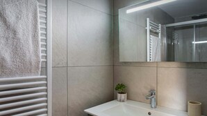 Un baño con un lavamanos blanco, un espejo, un perchero para toallas y una pequeña planta en maceta.