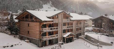 A multi-story wooden lodge with balconies, surrounded by snow-covered mountains.