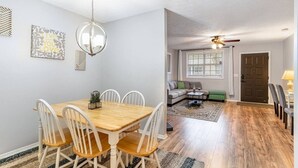 Ein Essbereich mit Holztisch und weißen Stühlen, einer Kandelaber und ein Wohnzimmer mit Sofa, Couchtisch und Deckenventilator.