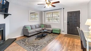 Ein Wohnzimmer mit grauem Sofa, Couchtisch, Kamin, Deckenventilator und einer Tür.