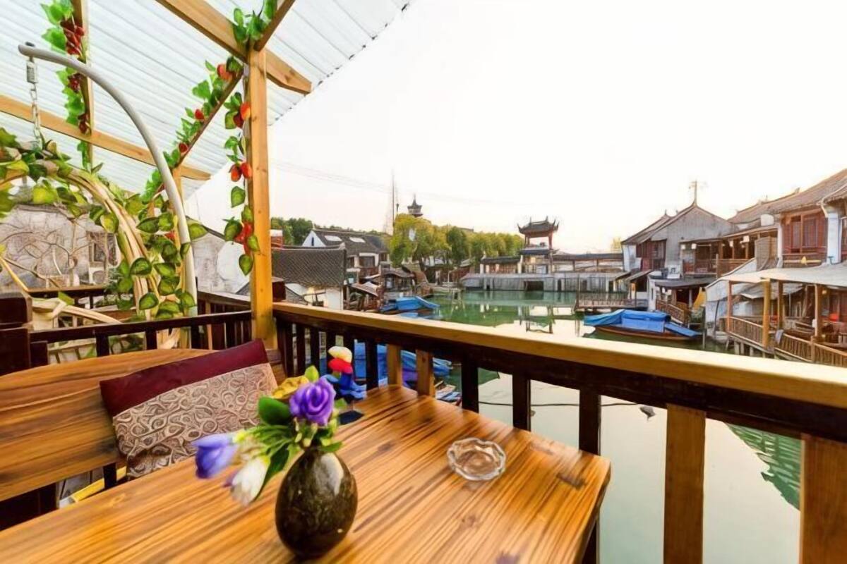 A wooden deck with a table, a vase with flowers, and a view of traditional buildings and water.