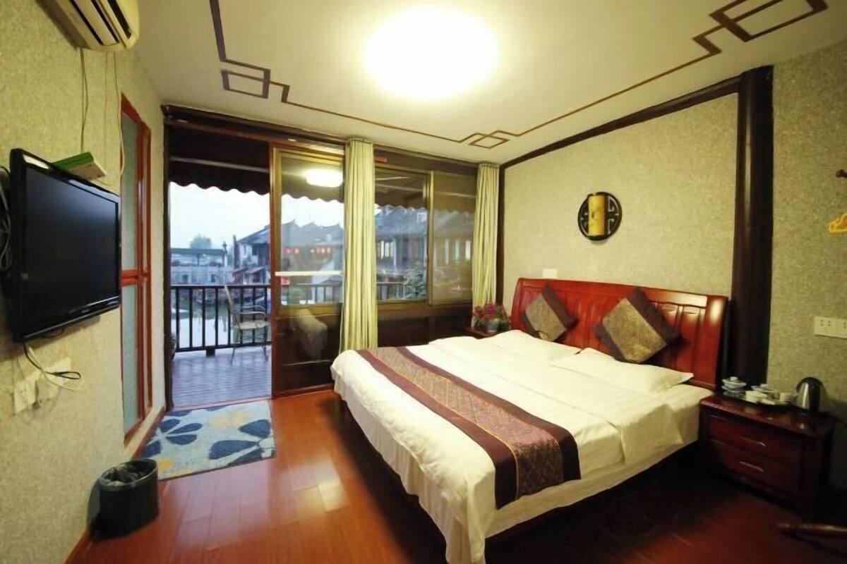 A hotel room with a bed, a TV, a balcony, and a view of buildings.