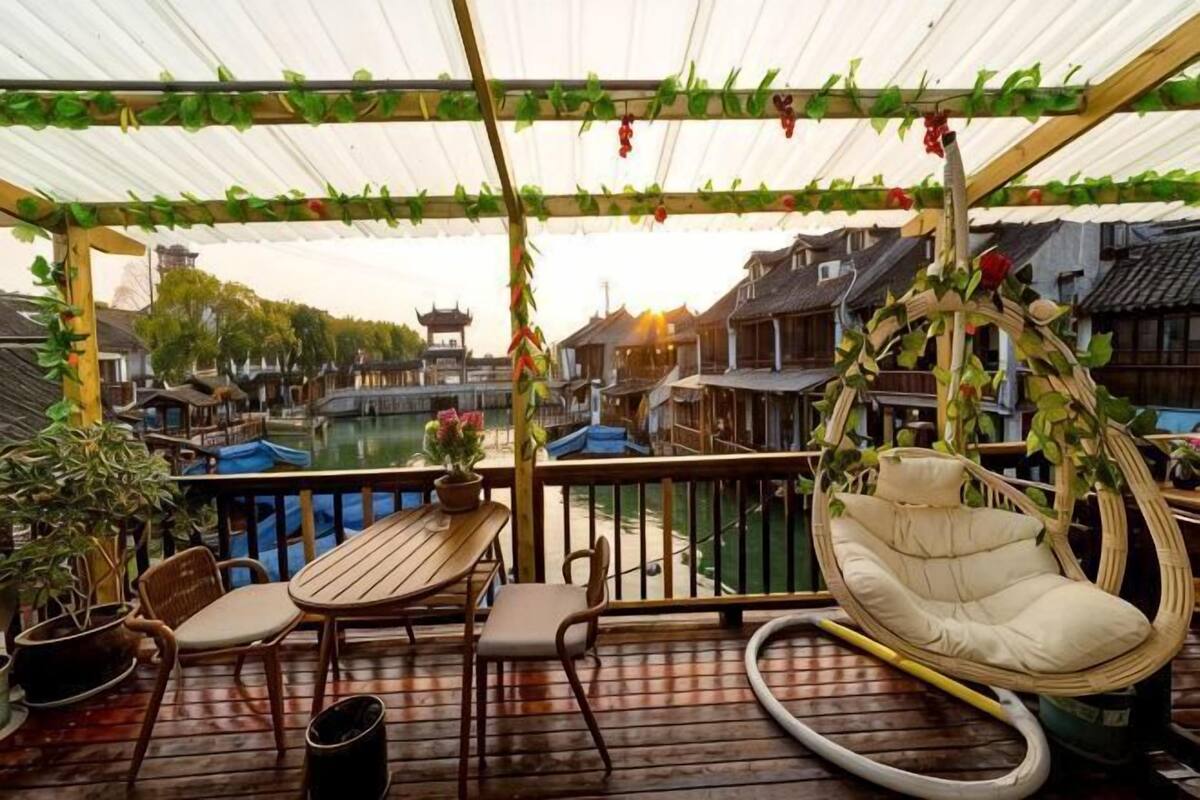 A covered outdoor area with a table and chairs, a hanging chair, and a view of traditional buildings and a canal.