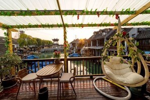 Een overdekt buitengebied met een tafel en stoelen, een hangstoel, en uitzicht op traditionele gebouwen en een gracht.
